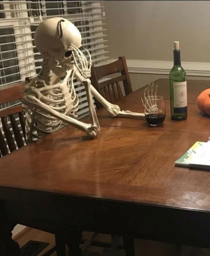 a skeleton sitting at a table next to a bottle of wine