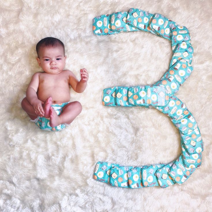 a baby in diapers sitting on a white rug next to the number five shaped like a snake