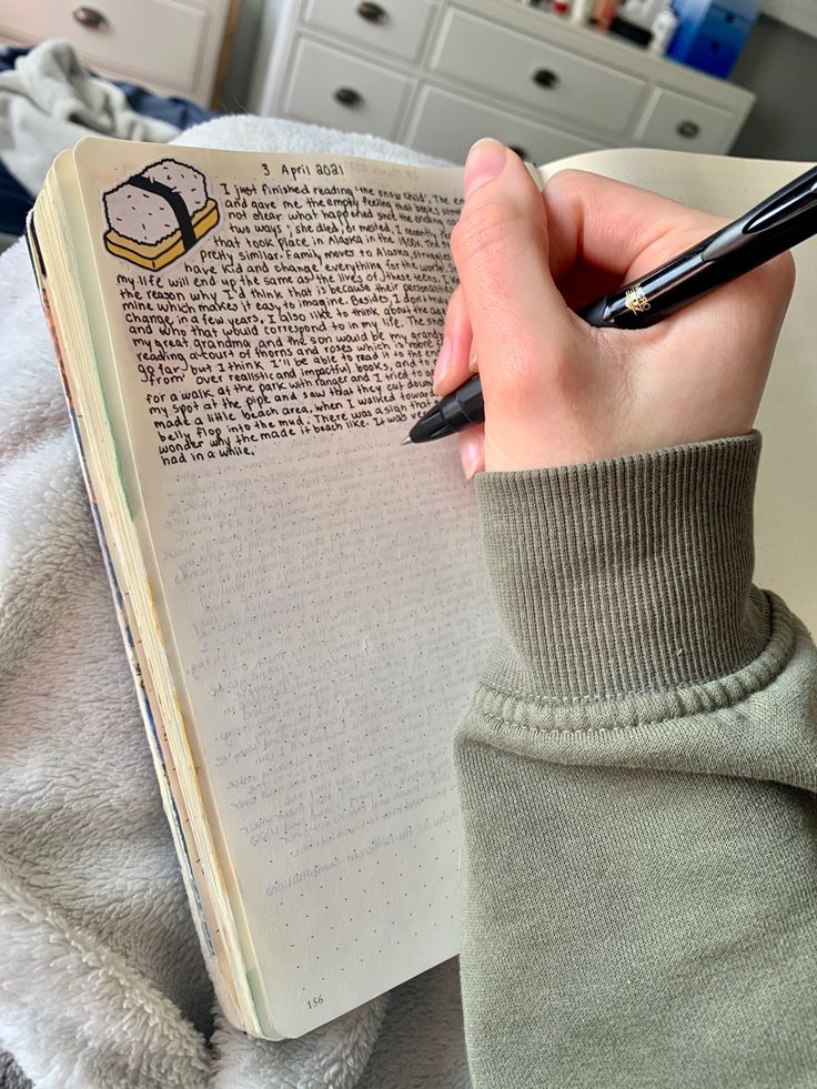 a person holding a pen and writing on an open book