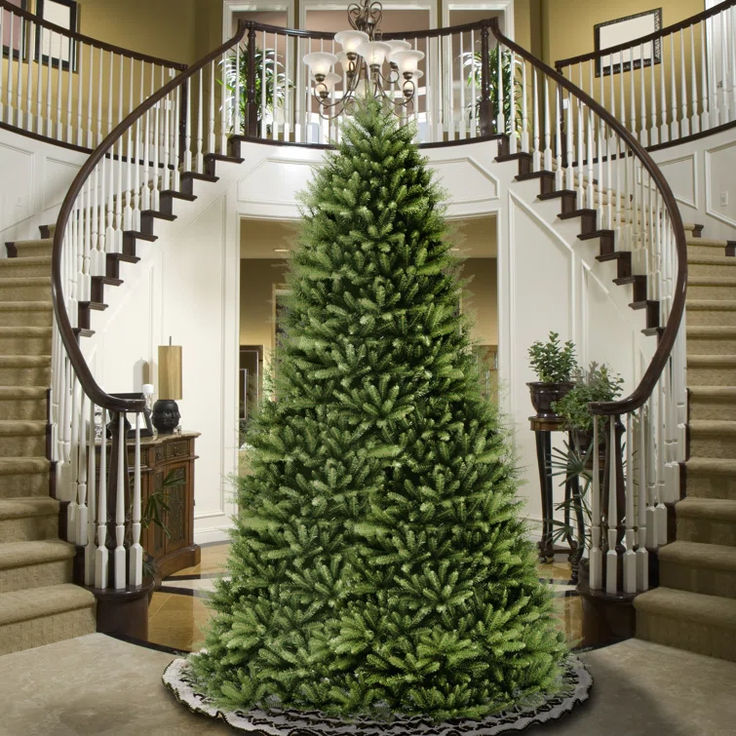 a large christmas tree in the middle of a room with stairs and chandelier