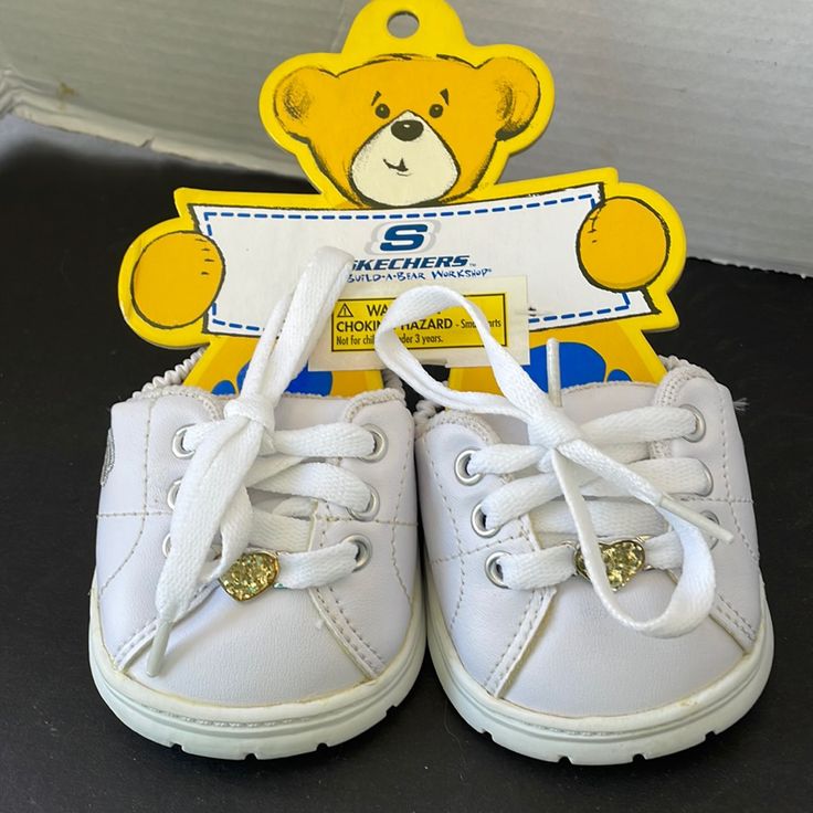 a pair of white tennis shoes sitting on top of a black table next to a yellow teddy bear