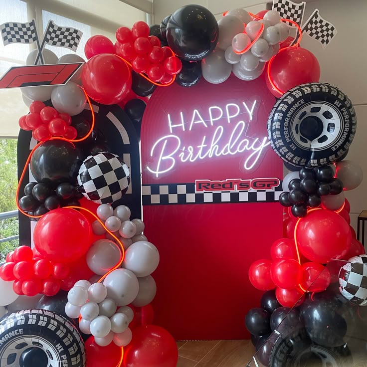 a happy birthday sign surrounded by balloons and race cars in front of a red backdrop