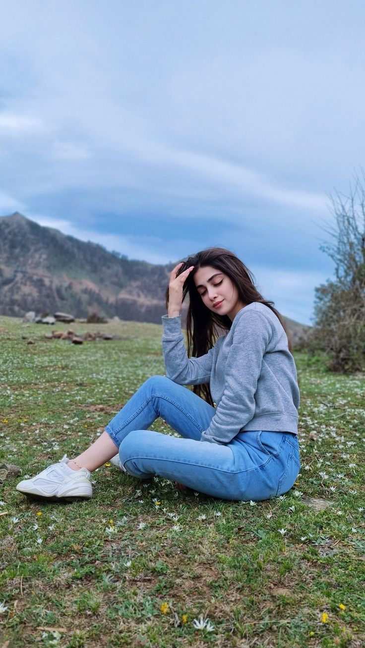 a young woman sitting on the ground with her head in her hands, wearing jeans and a sweater