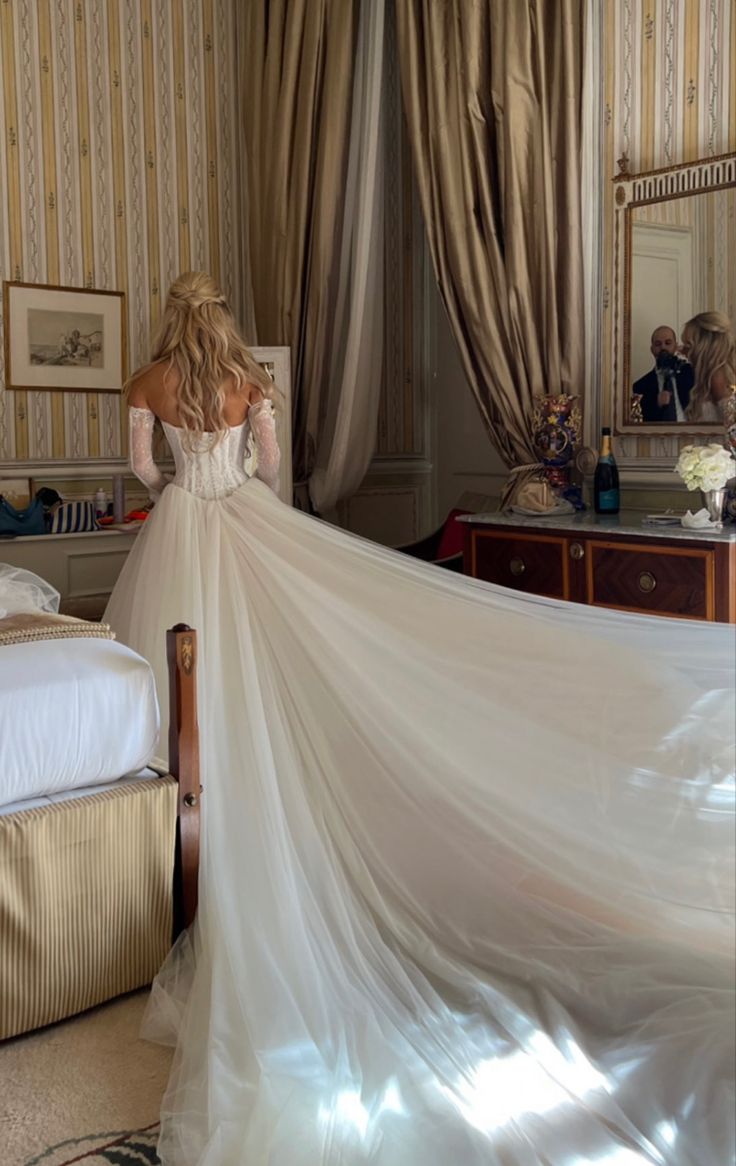 a woman in a wedding dress looking at herself in the mirror