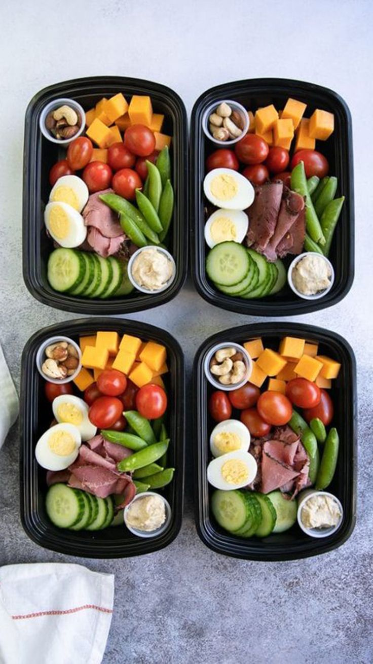 four black trays filled with different types of food on top of a gray table