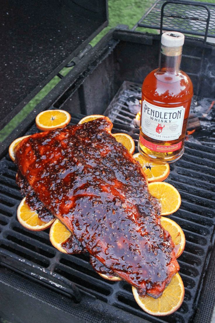 a bbq with ribs and orange slices on it next to a bottle of bourbon