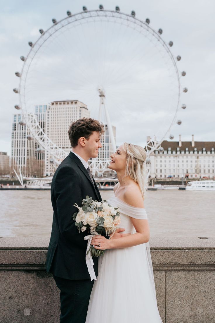 a bride and groom standing in front of the london eye