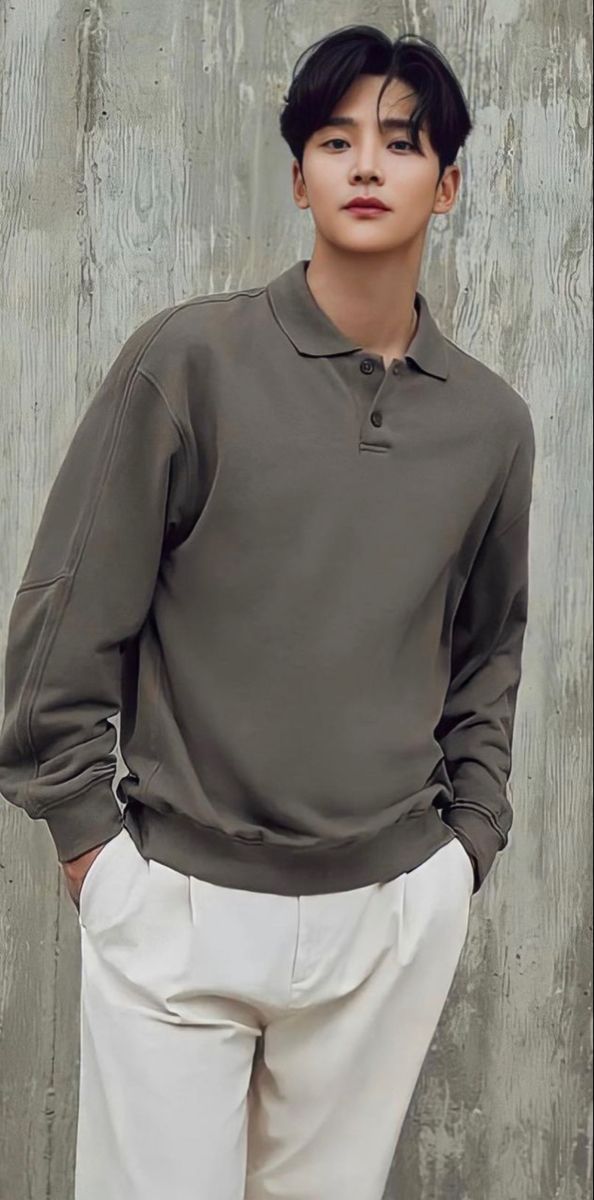 a man standing in front of a wall wearing a gray shirt and white pants with his hands on his hips