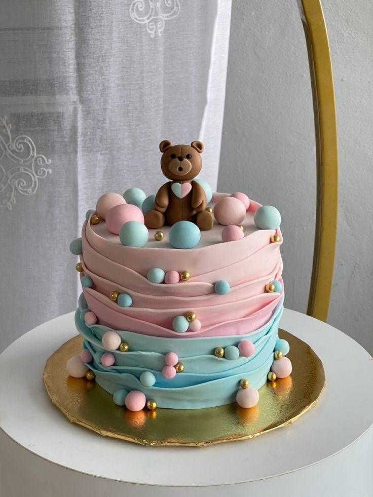 a teddy bear sitting on top of a multi layer cake with pink, blue and yellow frosting