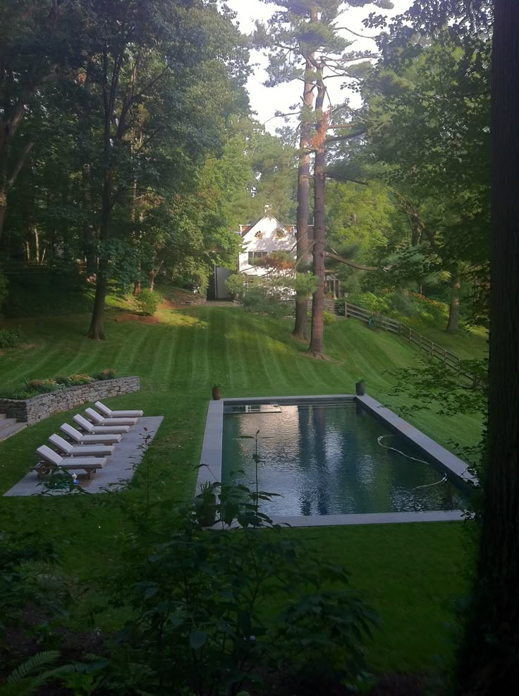 an empty pool in the middle of a lush green yard with lounge chairs around it