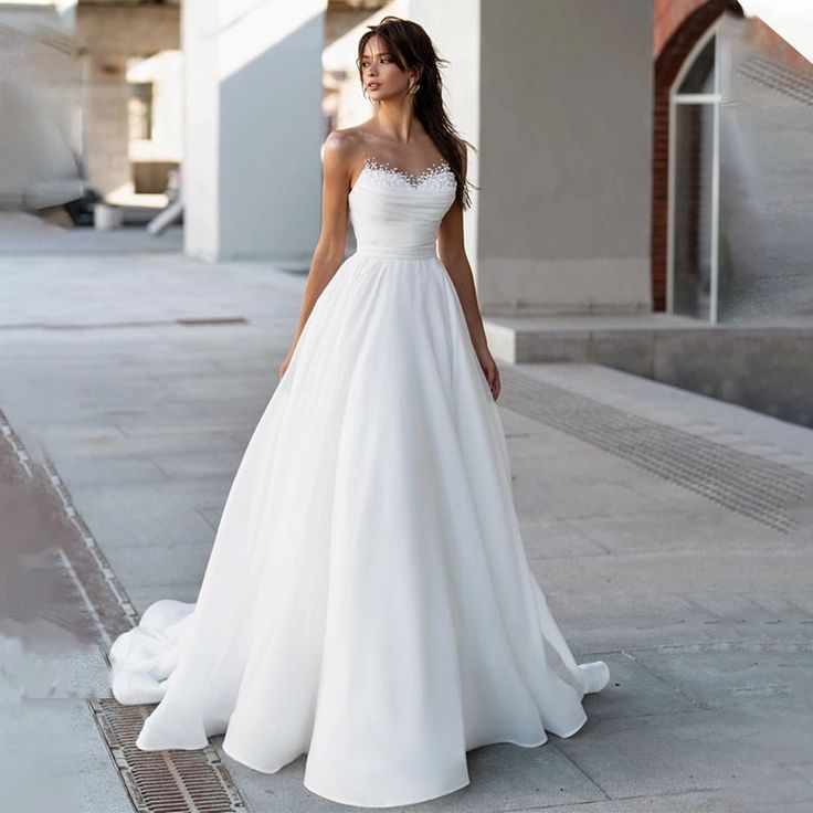 a woman in a white wedding dress is standing on the sidewalk and looking away from the camera