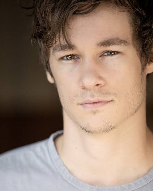 a close up of a person wearing a gray shirt and looking at the camera with a serious look on his face