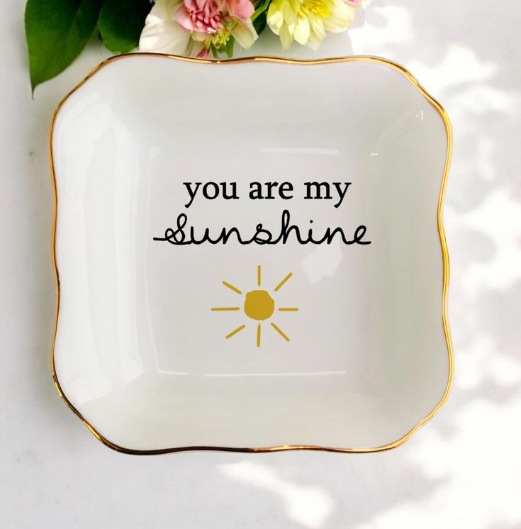 a white and gold plate with the words you are my sunshine on it next to flowers