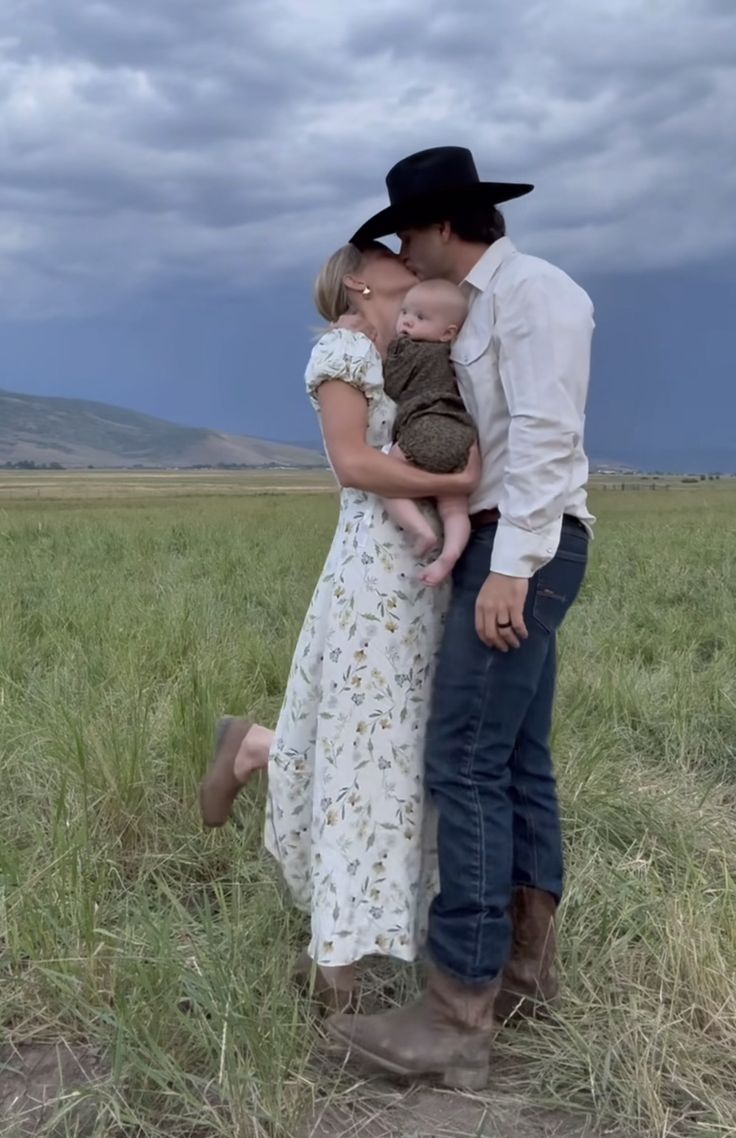 a man and woman kissing while standing in the middle of a field with a baby