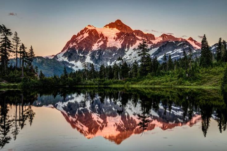 a mountain is reflected in the still water of a lake with trees on both sides