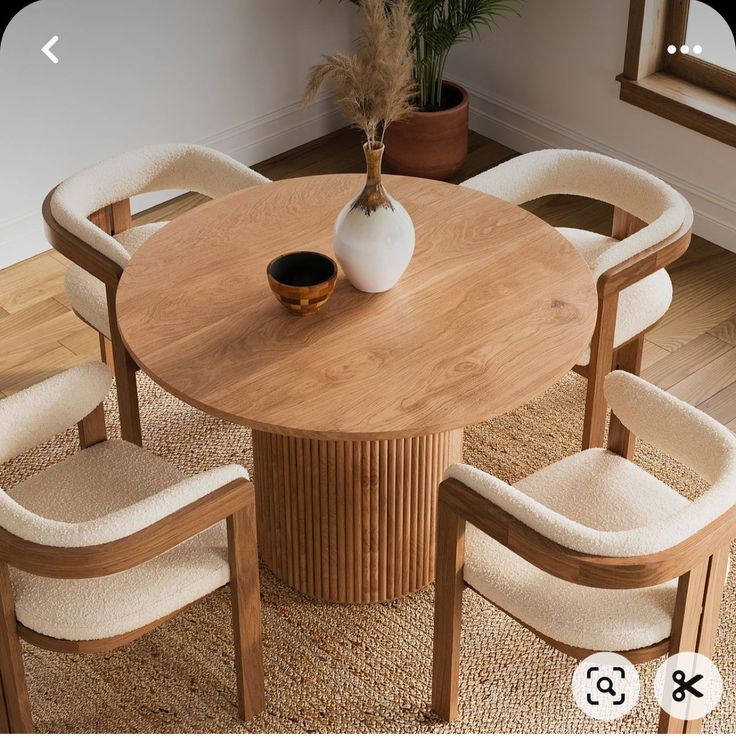 a round wooden table with four chairs around it and a vase on the table top