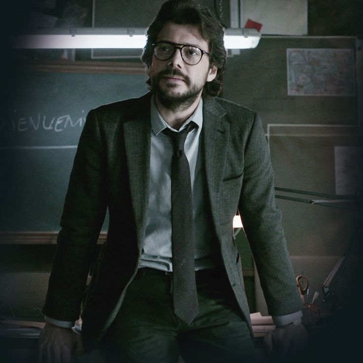 a man wearing glasses and a suit standing in front of a blackboard