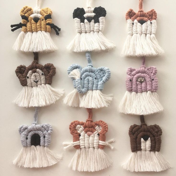 six small tassels are hanging on a white wall, each with an animal's head