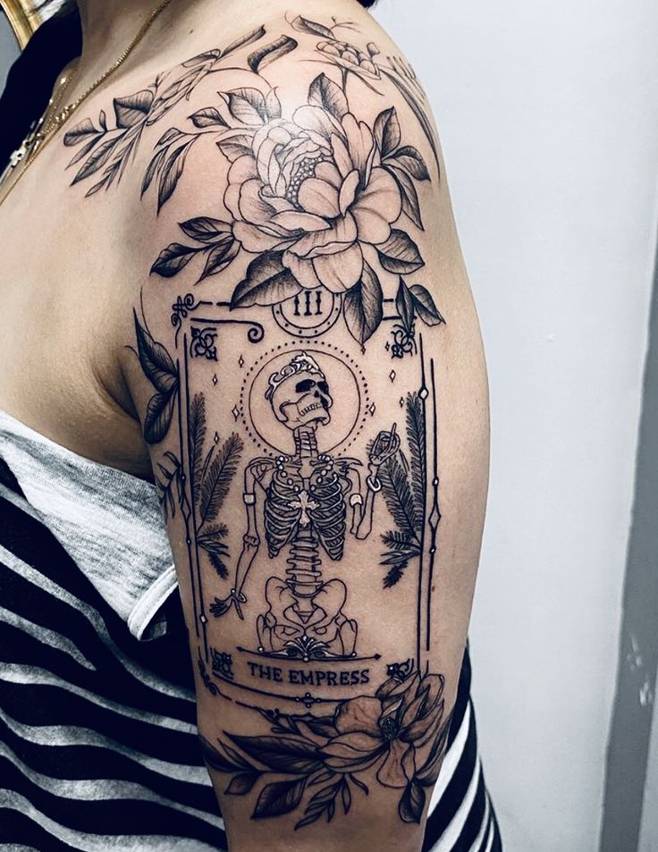 a woman's arm with a skeleton and flower tattoo on the left side of her shoulder