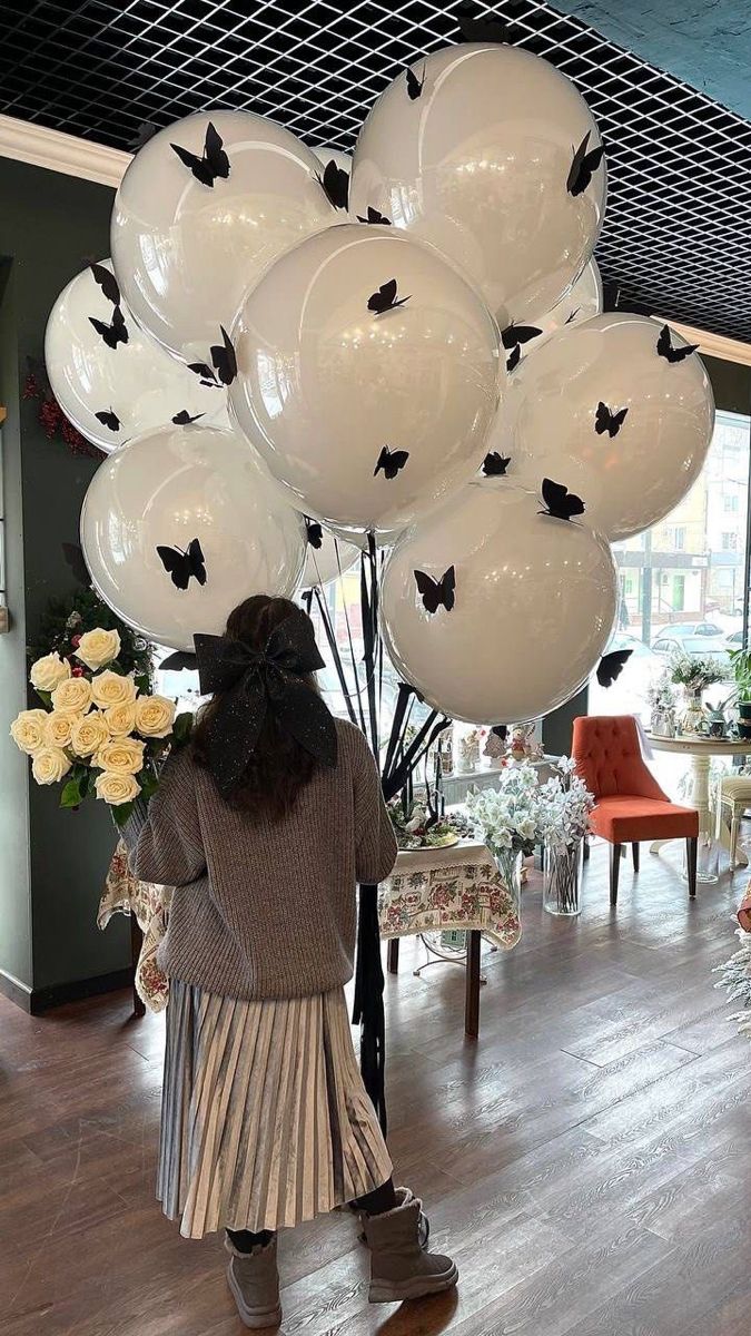 a woman standing in front of balloons that are shaped like bats and butterflies on the ceiling