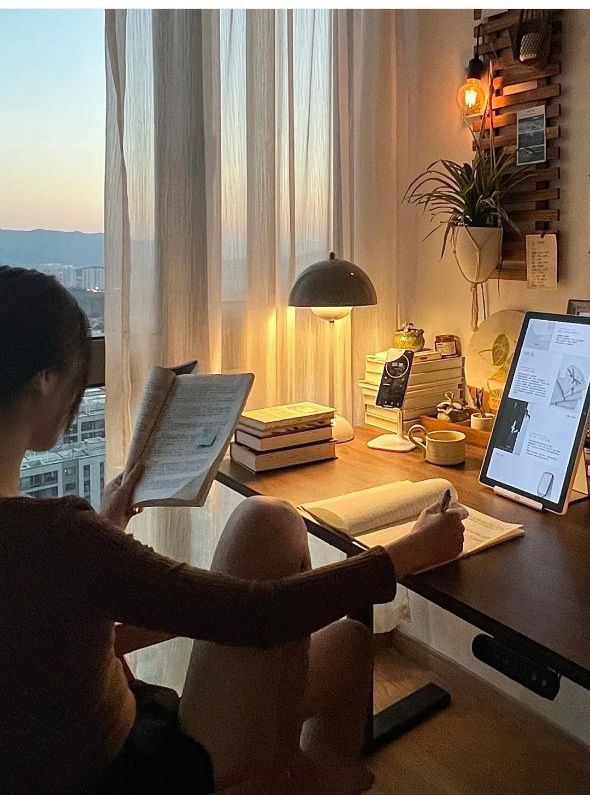 a woman sitting in front of a computer on top of a desk next to a window