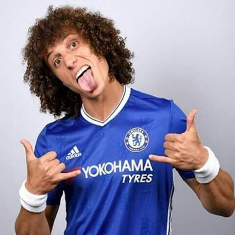 a man with curly hair making a funny face while wearing a blue soccer jersey and pointing his finger at the camera