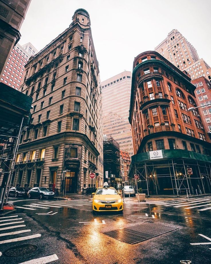 a yellow taxi cab driving down a wet street next to tall buildings in the city