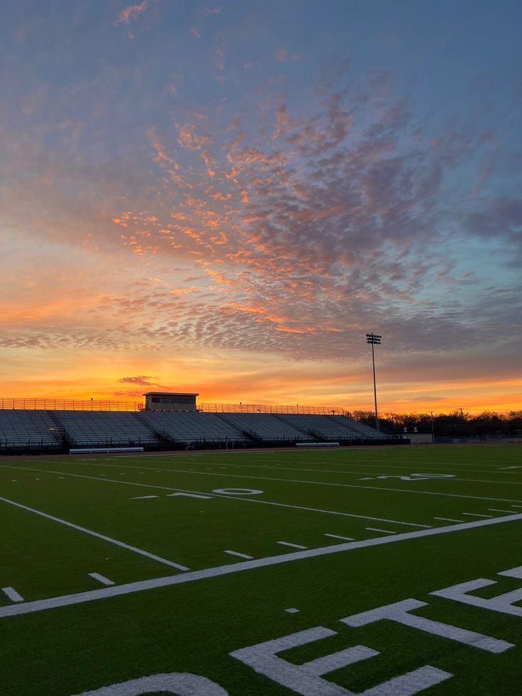 the sun is setting over an empty football field