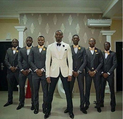 a group of men standing next to each other wearing suits and bow ties in front of a wall