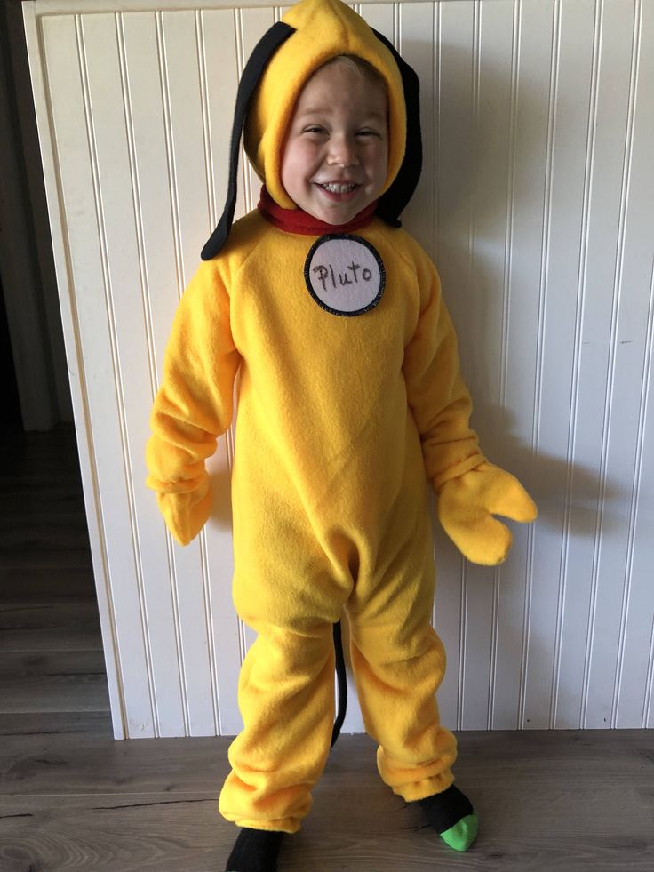 a young boy in a yellow costume standing next to a white wall and smiling at the camera