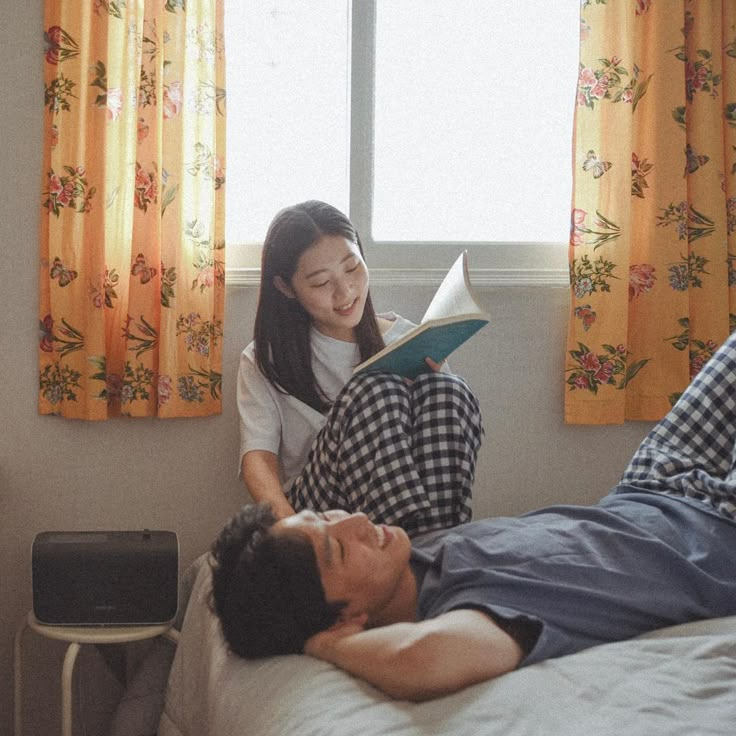 a man and woman are laying on a bed reading a book while looking at each other