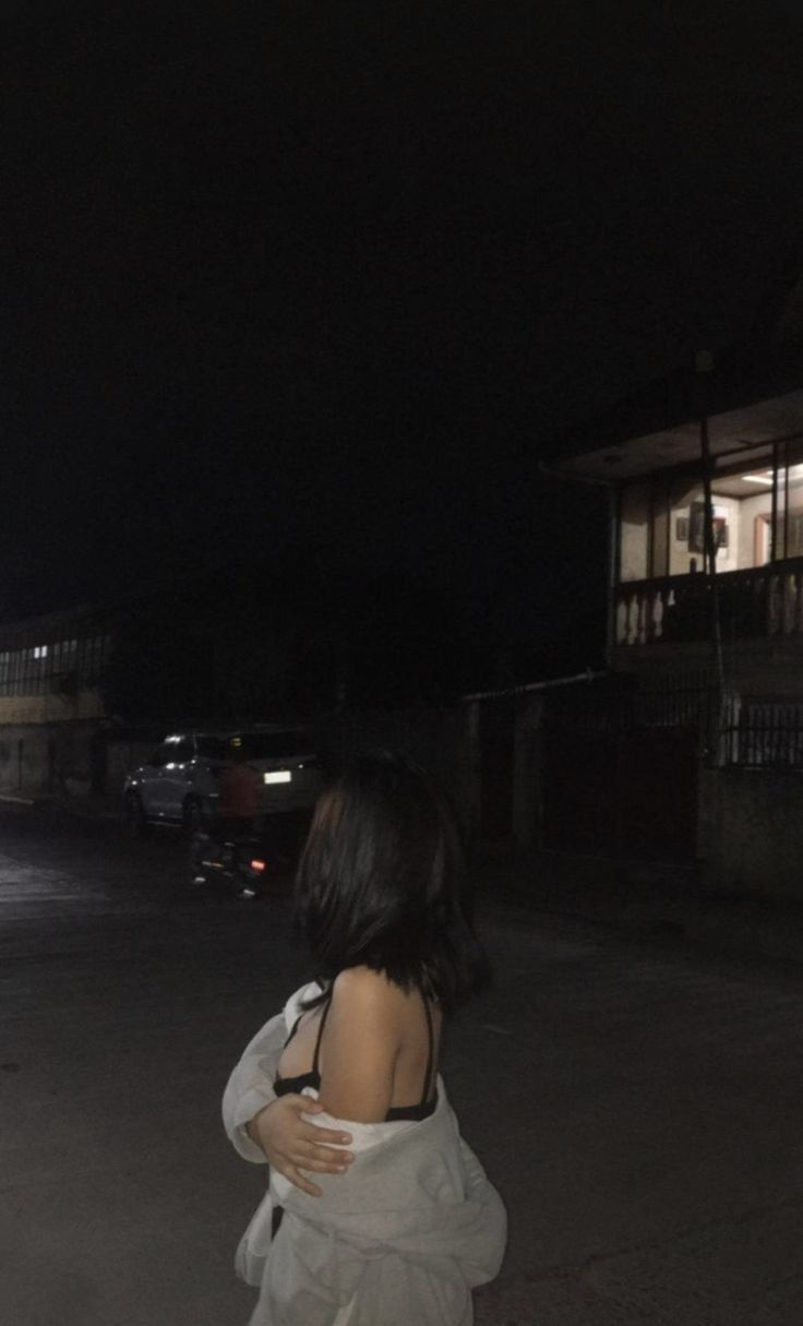 a woman standing in the middle of an empty parking lot at night with her back to the camera