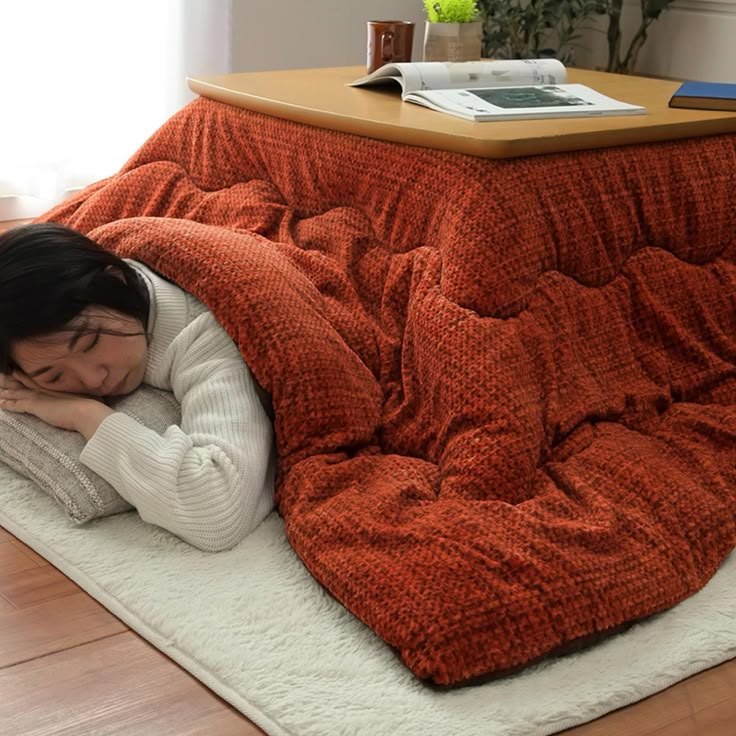 a woman is laying on the floor under an orange blanket and covering herself with her hands