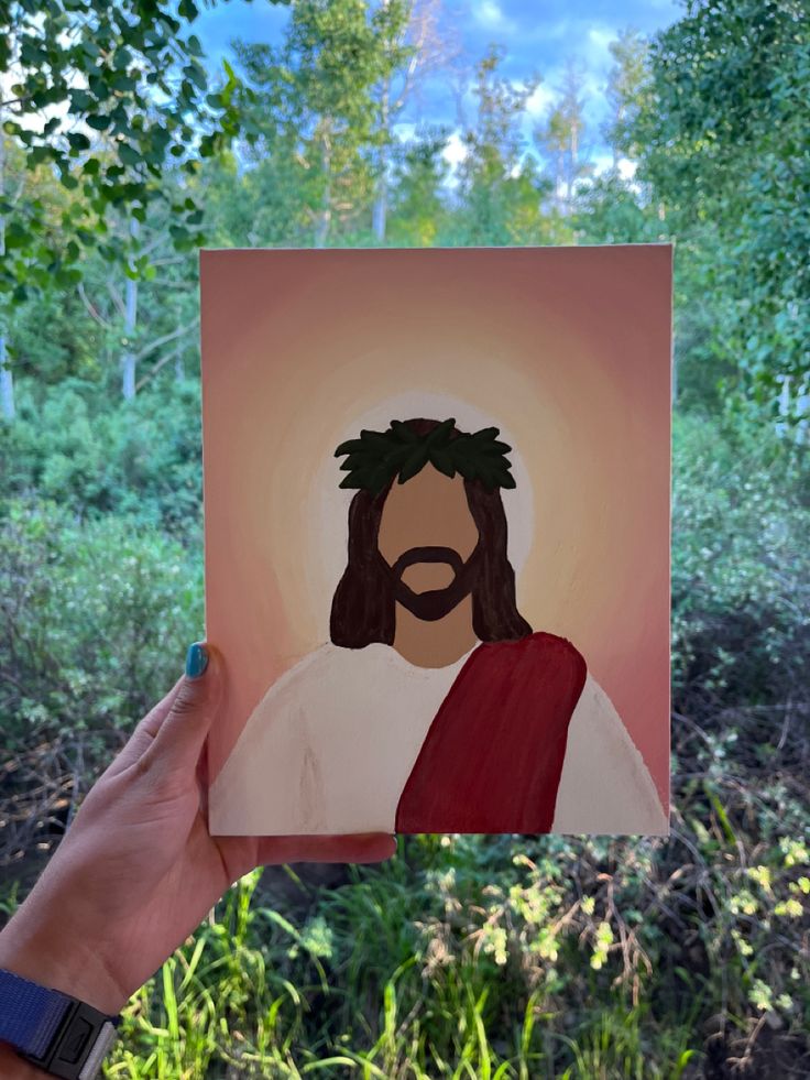 a hand holding up a paper cutout of jesus in the woods with trees behind it