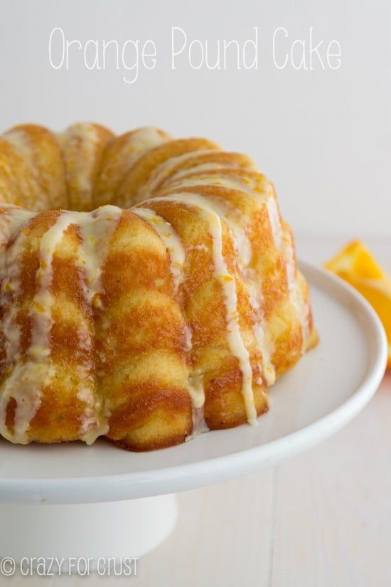 an orange pound cake with icing on a white plate next to sliced oranges