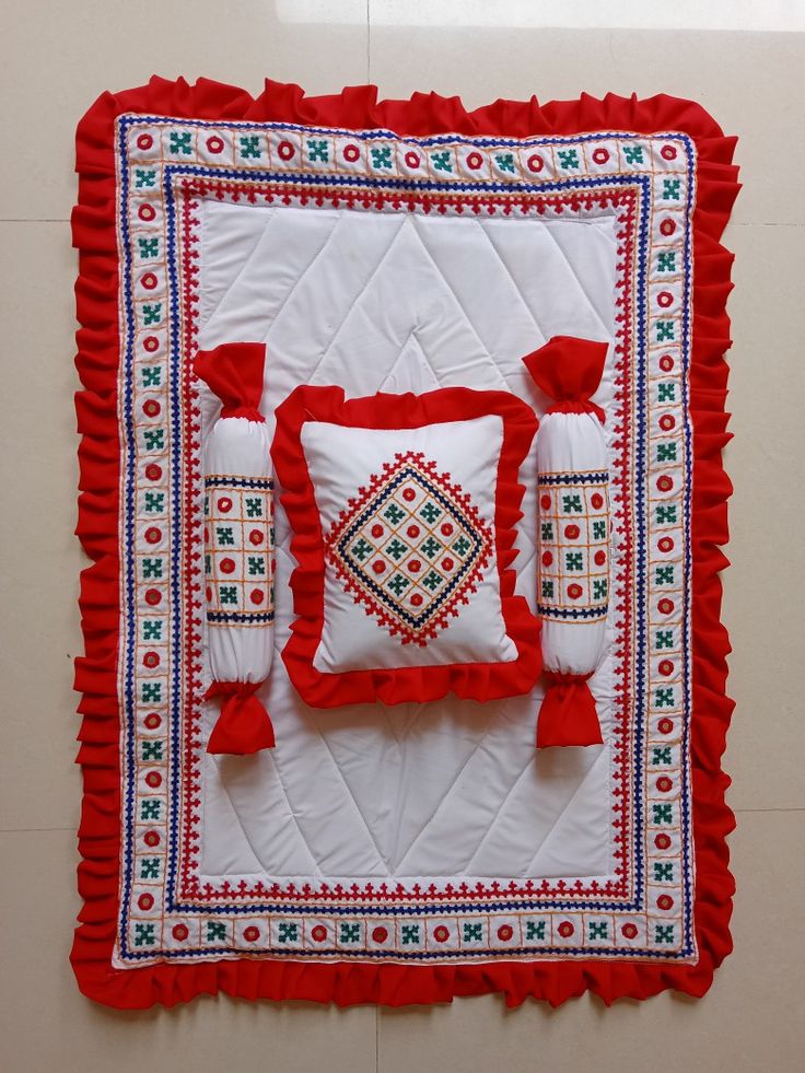 a red and white quilted wall hanging on the side of a wall next to pillows