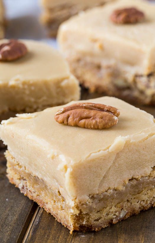 three pieces of cake with frosting and pecans on top sitting on a wooden surface