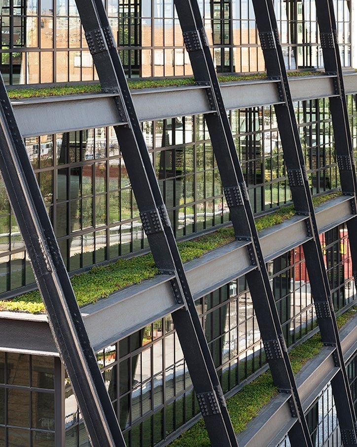 an office building with grass growing on the side of it's glass walls and metal railings