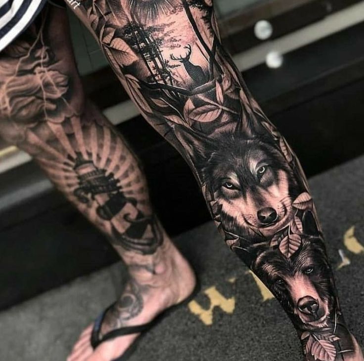 a man's leg with tattoos and an image of a wolf in the woods