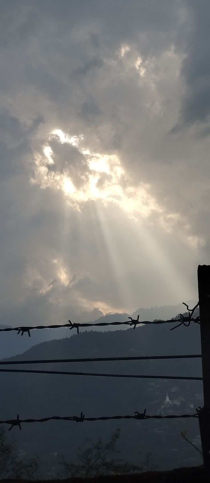 the sun is shining through the clouds behind a barbed wire fence