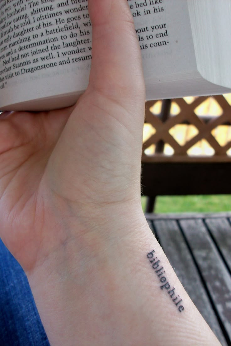 a person with a book tattoo on their wrist holding an open book in front of them