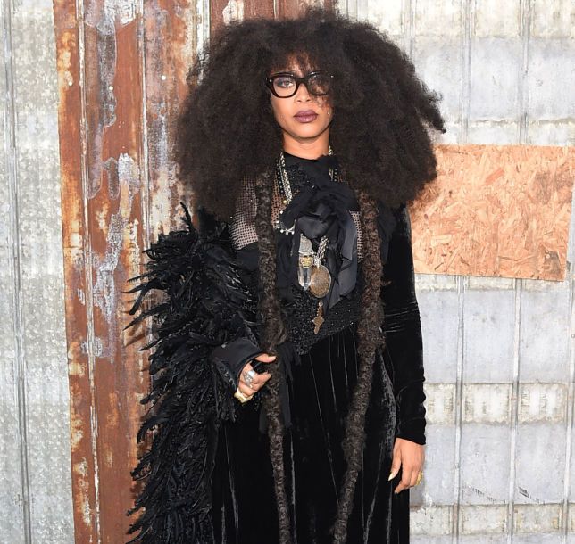 a woman with long hair and glasses standing in front of a wooden door wearing a black dress