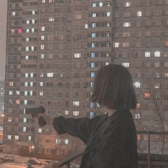 a woman standing on top of a balcony next to a tall building at night time