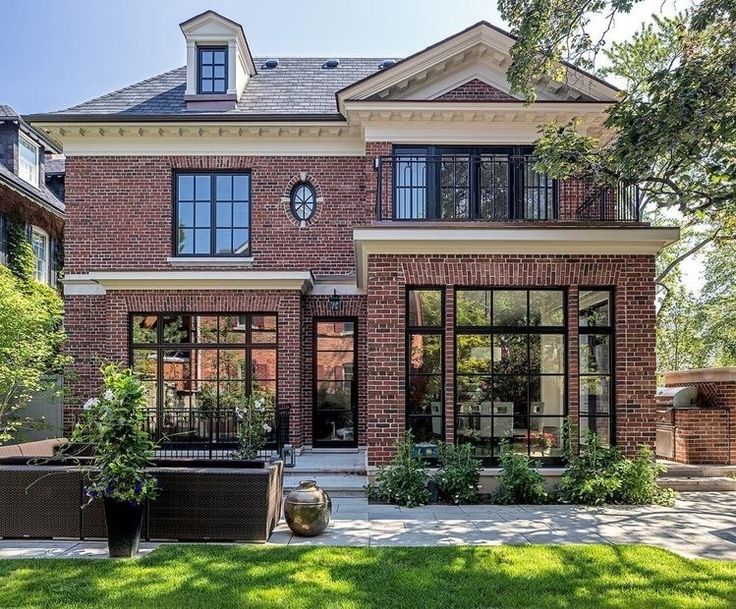 a large brick house with lots of windows and plants in the front yard, on a sunny day