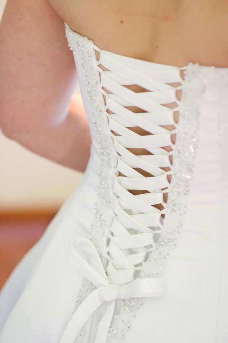 the back of a bride's wedding dress with a white ribbon tied around it