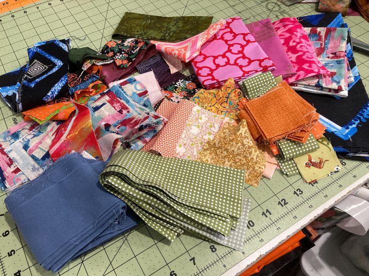 many pieces of fabric are laid out on a cutting board to be sewn together