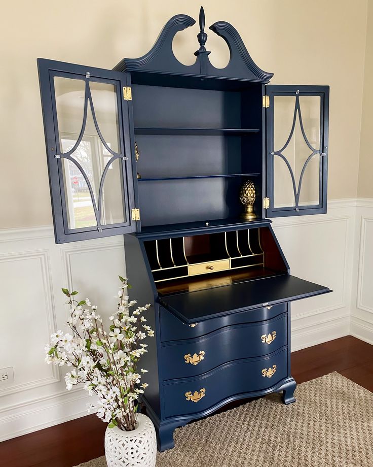 a blue desk with an open bookcase on top and flowers in vase next to it