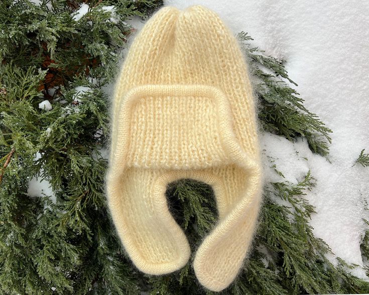 a knitted hat laying on top of snow next to evergreen branches and pine needles