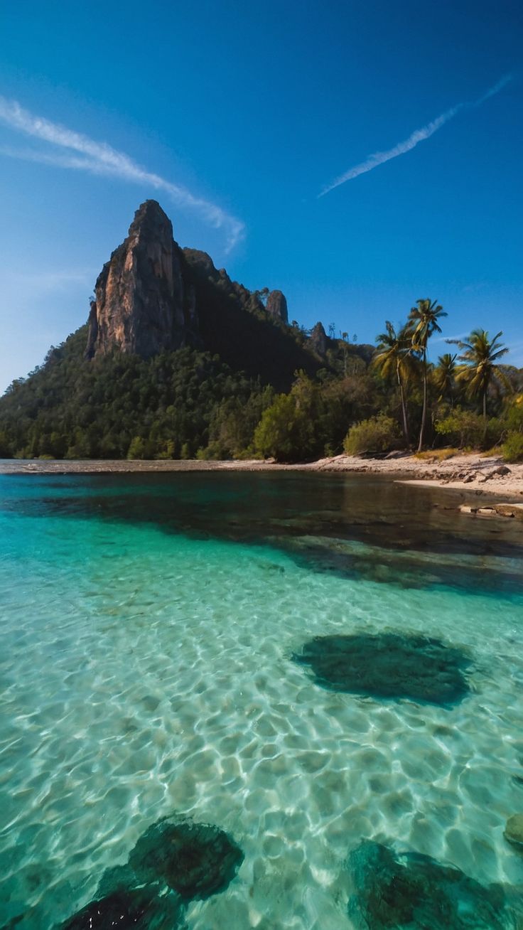 the water is crystal clear and there are some rocks in the foreground with mountains in the background