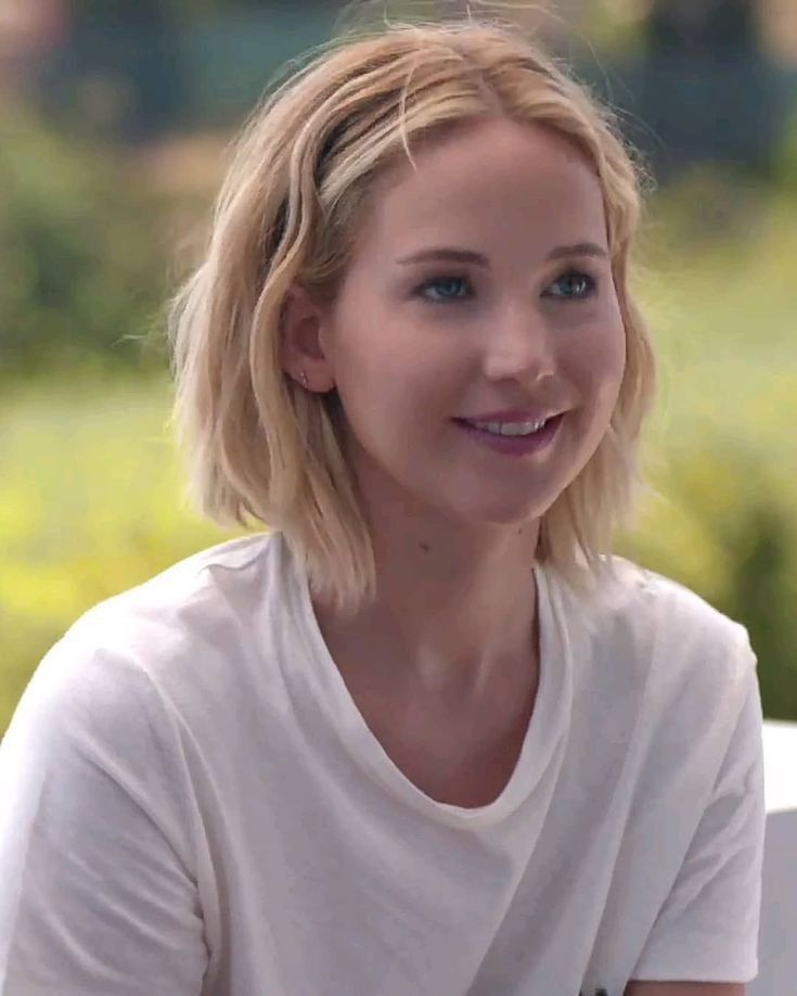 a woman with blonde hair and blue eyes smiles at the camera while wearing a white t - shirt